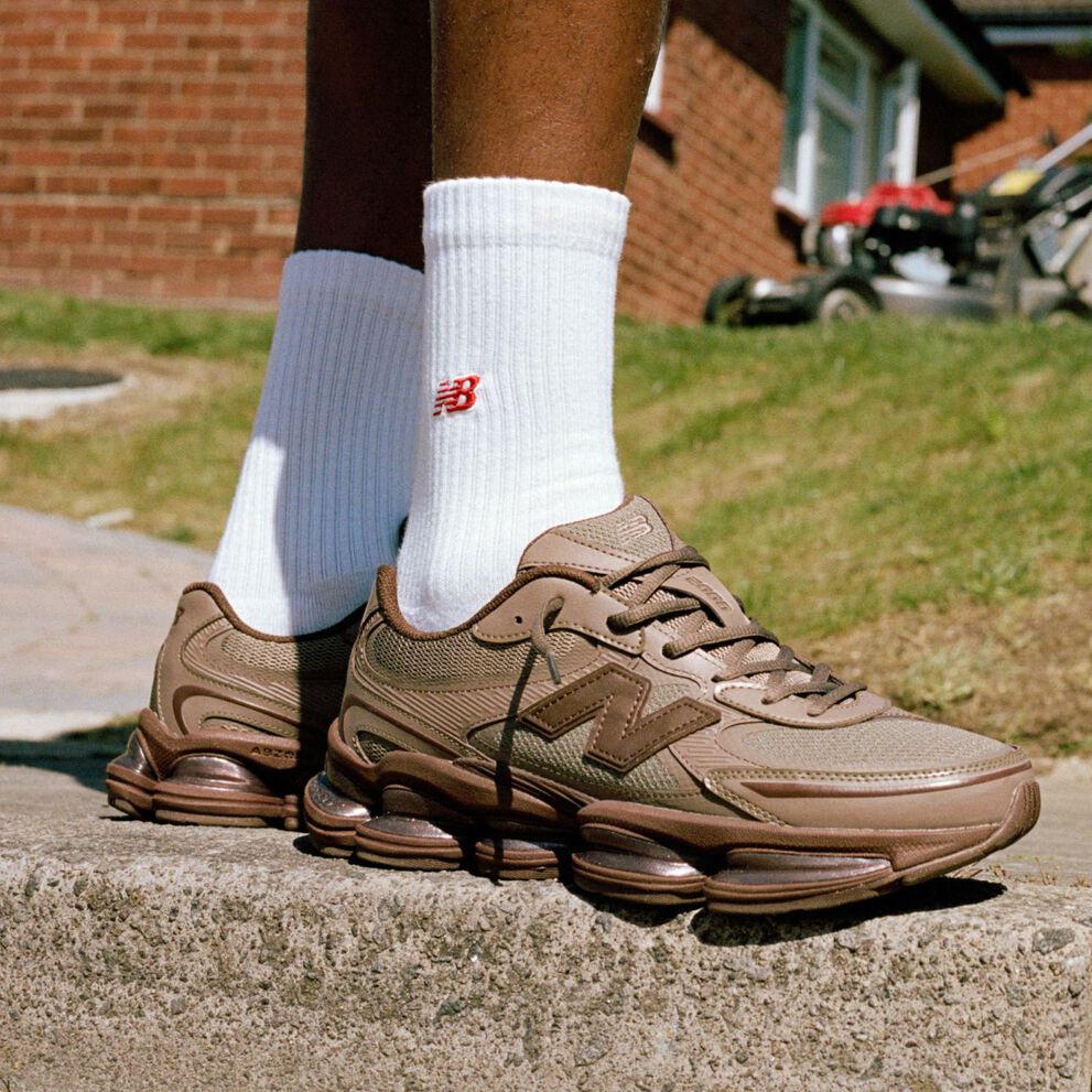 Knee-down image of someone wearing brown New Balance sneakers outdoors.